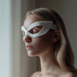 3D printed minimalist eye mask glasses with sculptural cutout frames worn by an adult woman standing by a window in soft daylight.