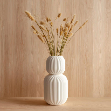 Tall 3D printed white geometric vase with ribbed texture, holding dried grass stems, displayed against a light wood background