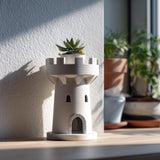 3D printed planter shaped like a small castle tower or rook, holding a succulent on a windowsill, with soft natural light and other plants in the background.