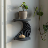 3D printed double-tier spiral wall shelf in matte dark PLA, with a twisting ribbed support between two round shelves, styled with small decor in a modern interior.