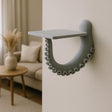 A sculptural 3D printed wall shelf designed to resemble a curled octopus tentacle with suction cups, mounted on a neutral wall in a coastal-style living room.