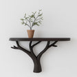 Black 3D printed wall shelf shaped like branching tree limbs, mounted on a white wall and holding a terracotta potted plant.