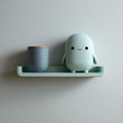 3D printed wall shelf with a slim rounded ledge holding a small blob-like character and a cup, made from matte PLA plastic and mounted on a light-colored wall.