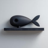 3D printed matte PLA wall shelf with a stylized fish figure resting on a slim rectangular ledge, mounted on a light-colored wall.