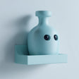Cute 3D printed matte PLA wall shelf with an integrated kawaii potion bottle character, in soft pastel blue, mounted on a flat light-colored wall.