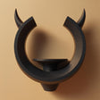 3D printed matte PLA wall shelf shaped like an open ring with two upward horns and a small round pedestal ledge in the center, mounted on a warm-toned wall.
