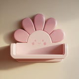 3D printed kawaii flower wall shelf with rounded petals, a smiling face, and a small floating ledge, mounted on a softly lit interior wall.