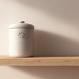 Minimalist 3D printed pet cremation urn with subtle paw print detail, placed on a wooden floating shelf against a soft neutral wall.