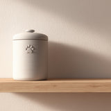 Minimalist 3D printed pet cremation urn with subtle paw print detail, placed on a wooden floating shelf against a soft neutral wall.
