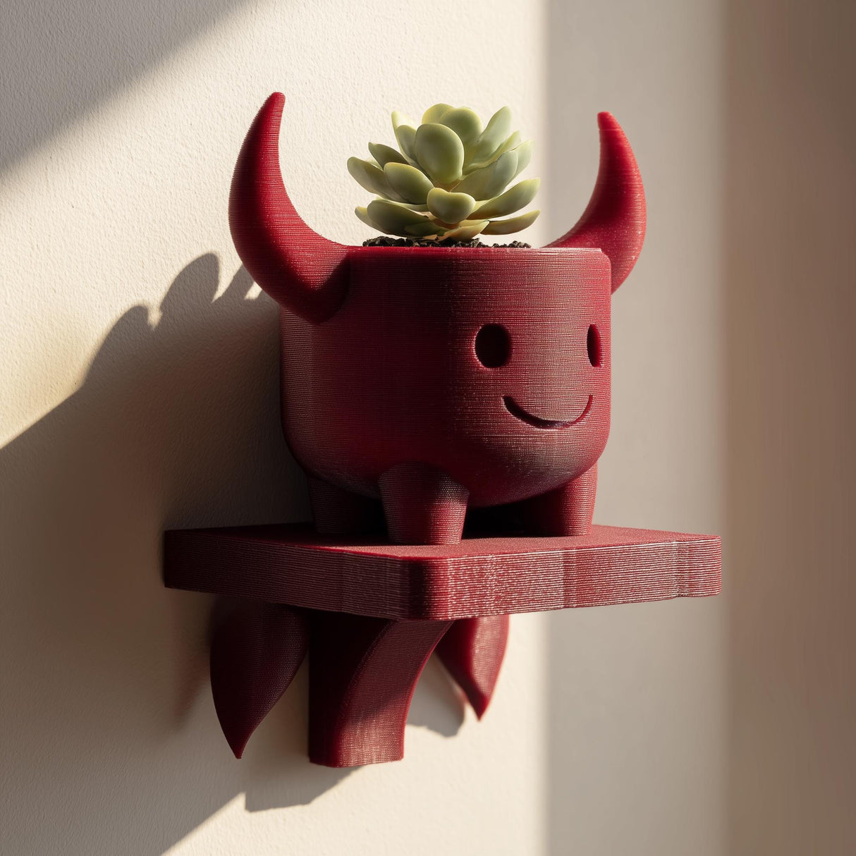 Wall-mounted 3D printed planter shelf featuring a cute red devil-shaped pot holding a small succulent, designed as playful fantasy wall decor.