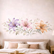 A horizontal watercolor illustration of three lilies in a row on a white background. From left to right: a light purple lily, a soft pink lily, and a warm peach lily. The flowers are connected by a central horizontal stem with delicate, pale green and grey leaves.
