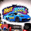 A 3D-effect illustration of a vibrant blue sports car bursting through a white brick wall. The car features "BOOST" and "FAST" decals on its side. Above the car, the words "FAST BOOST" are written in large, colorful graffiti letters against a dark, star-filled background visible through the jagged wall crack.