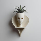 3D printed wall mounted face planter shelf with integrated pot, sculptural minimalist design holding a small plant on a neutral wall.