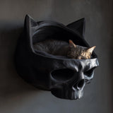 3D printed dark fantasy skull wall mounted cat bed in matte black PLA with a sleeping tabby cat inside, gothic interior setting.