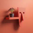 3D printed modern character wall shelf with abstract face design and integrated horizontal shelf, mounted on a warm terracotta colored interior wall.