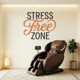 A wall decal that reads STRESS Free ZONE. The words STRESS and ZONE are printed in large, dark charcoal grey block letters. The word Free is positioned between them in an elegant, flowing, terracotta-colored cursive script. The text is applied directly to a smooth, light-colored wall, creating a clean, painted-on appearance. The surrounding settings include a plush brown massage chair, a modern office meeting room, and a serene yoga space, suggesting a peaceful, relaxing environment.