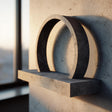 3D printed wall mounted shelf with a bold circular arch ring back and a slim floating ledge, shown against a textured wall near a window in warm light.