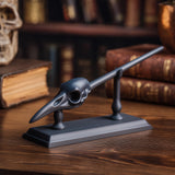 3D printed raven skull magic wand with display stand in matte black PLA on a wooden desk surrounded by gothic fantasy decor.