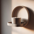 3D printed wall mounted memorial shelf with cylindrical urn in matte PLA featuring minimalist circular frame design on warm neutral wall.