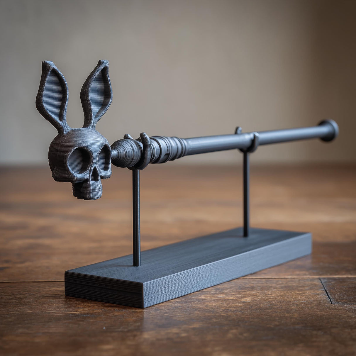 3D printed rabbit skull magic wand with long ears and display stand in matte black PLA on a wooden table in a fantasy interior.