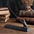 3D printed raven magic wand with matching display stand in matte PLA displayed on a wooden desk with vintage books and gothic decor.