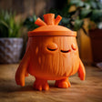 3D printed cute goblincore woodland memorial urn with tree stump character design and removable lid displayed on a wooden table.