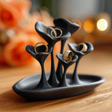Black 3D printed mushroom-style jewelry holder with curved cup-shaped ring holders on a tray base, displayed on a wooden surface with gold rings inside.