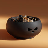 Pumpkin-shaped jewelry organizer bowl with cutout-style eyes and nose, filled with rings and small jewelry on a warm studio background.