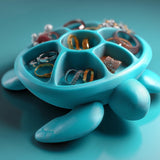 Sea turtle-shaped jewelry organizer with divided shell compartments holding rings and small jewelry on a smooth surface with an ocean-inspired background.