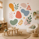 Abstract botanical design on a white background with sage and dark green leafy branches, coral and mustard foliage, rounded pink, blue, green and orange shapes, and small colored dots.