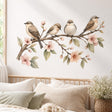 Watercolor illustration of four small brown, taupe, and cream birds perched on a flowering branch with blush pink blossoms, delicate buds, and muted green leaves on a white background.