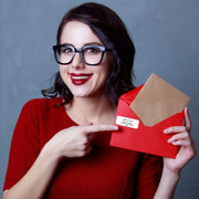Woman with glasses holding a red envelope featuring a personalized mailing label.