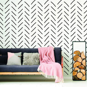 Stylish herringbone wallpaper in black on a white wall behind a cozy seating area with cushions and a pink throw.