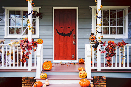 Halloween entrance featuring a scary smile door decal, pumpkins, and festive fall decorations.